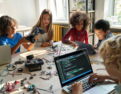 Diverse school children students build robotic cars using computers and coding.