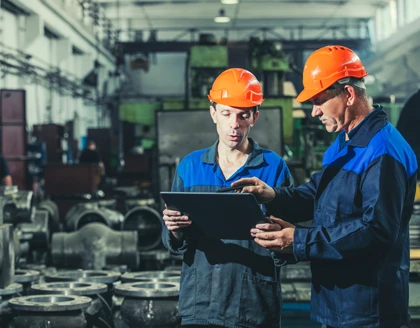Two workers at an industrial plant with a tablet in hand.